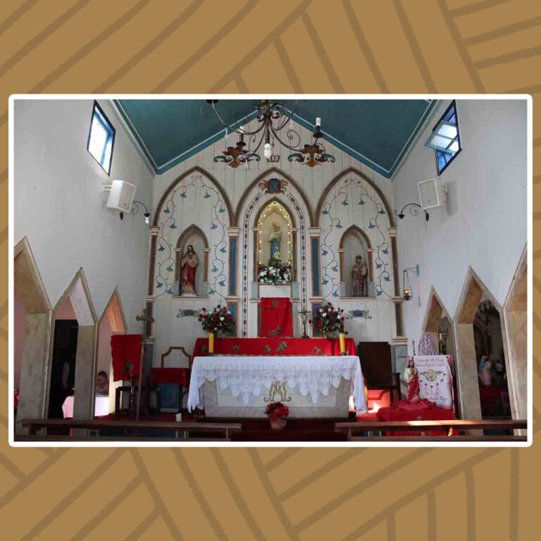 Para todos verem: Altar Mor da Capela de Nossa Senhora do Rosário. O forro da Capela, em formato triangular azul-escuro, se contrapõe com as paredes laterais e o fundo do altar mor, ambos em de cor branca. O altar é composto por três imagens, cada uma envolta por um arco triangular dourado de base em colunas azuis. À esquerda, imagem do Sagrado Coração de Jesus. À Direita, imagem de São José. Ao centro, imagem de Nossa Senhora do Rosário. À frente do Altar Mor, a mesa da eucaristia com toalha de mesa branca. Ao fundo, Sacrário envolto por toalhas vermelhas. No teto, Um lustre içado ao centro da capela.
