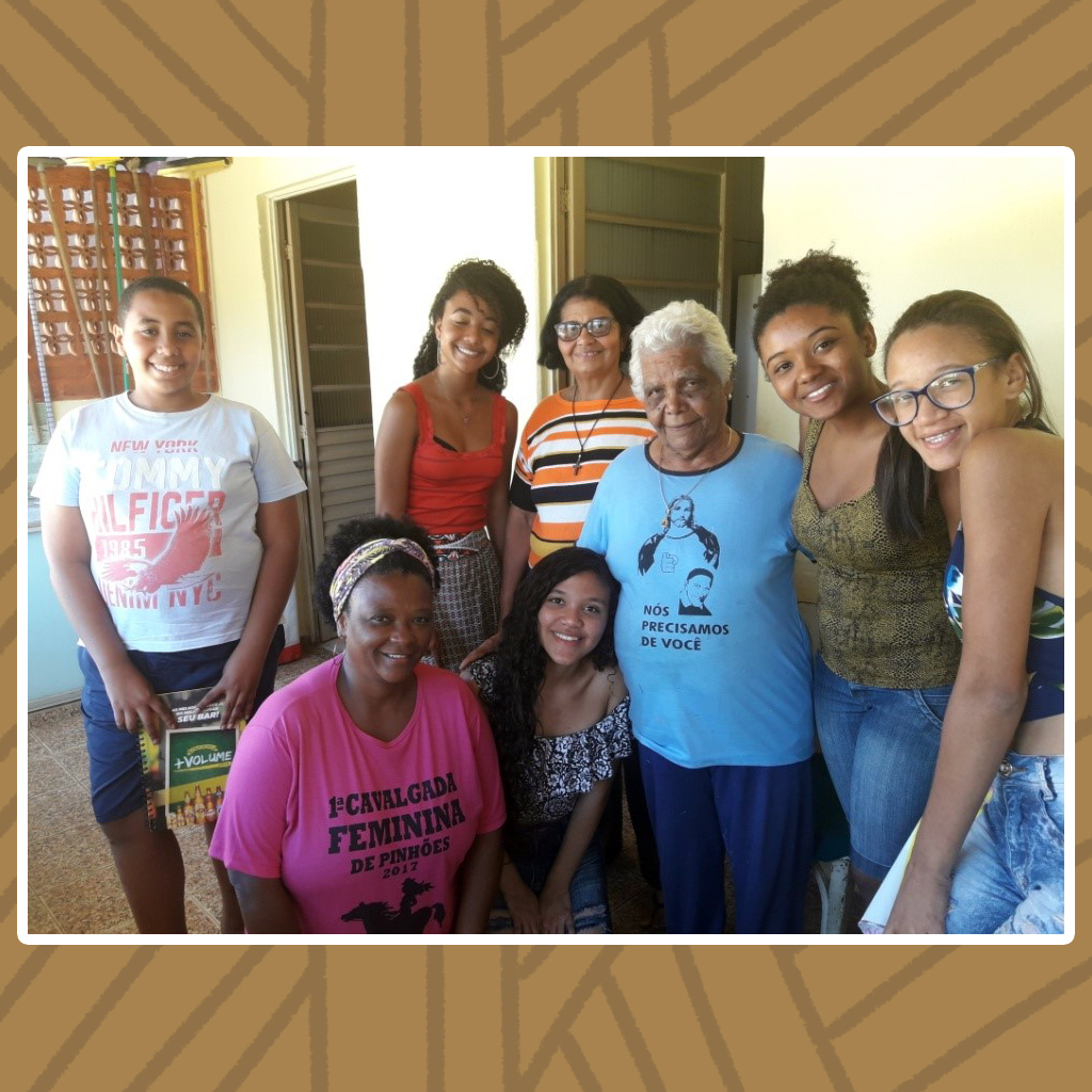 Grupo composto por cinco jovens, sendo quatro moças e um rapaz. Três senhoras são abraçadas pelo grupo.