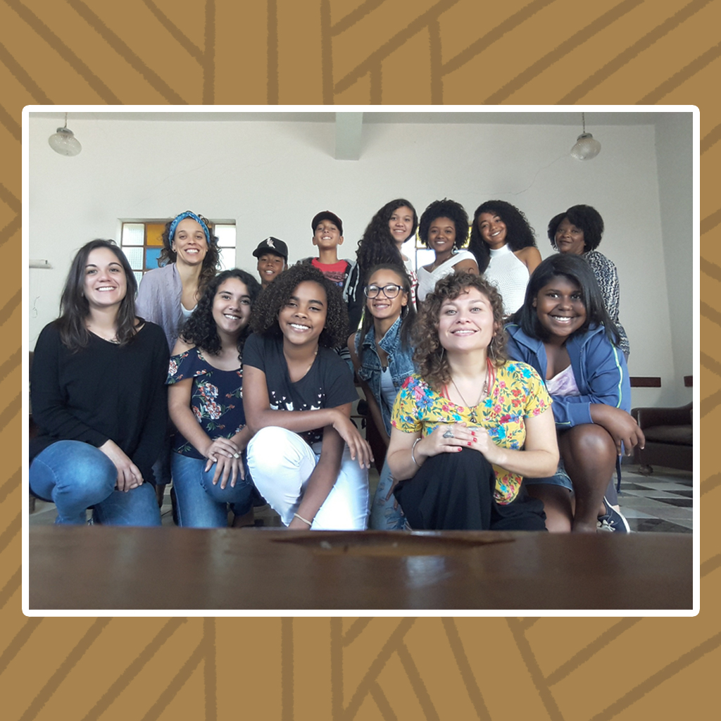 Em um salão de paredes brancas e piso quadriculado em vários tons de cinza, jovens mulheres quilombolas posam para a foto. São aproximadamente 11 mulheres, a maioria delas agachadas e algumas de pé. Destaque para os variados tipos de penteados e cabelos, que vão do liso, passando pelo cacheado e crespos. Todas exibem largos sorrisos.